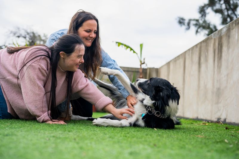 Wide view of mother and daughter with down syndrome playing outdoor with dog