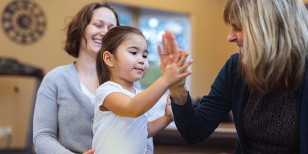 Child giving a high five to an adult while another adult watches.