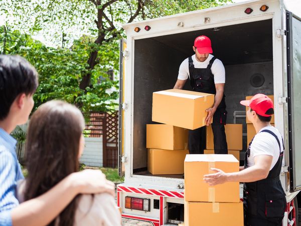 Two movers unloading boxes from a truck as a couple watches.