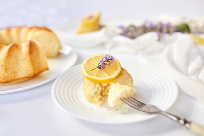 Piece of lemon cake on white table with lavender flower bouquet