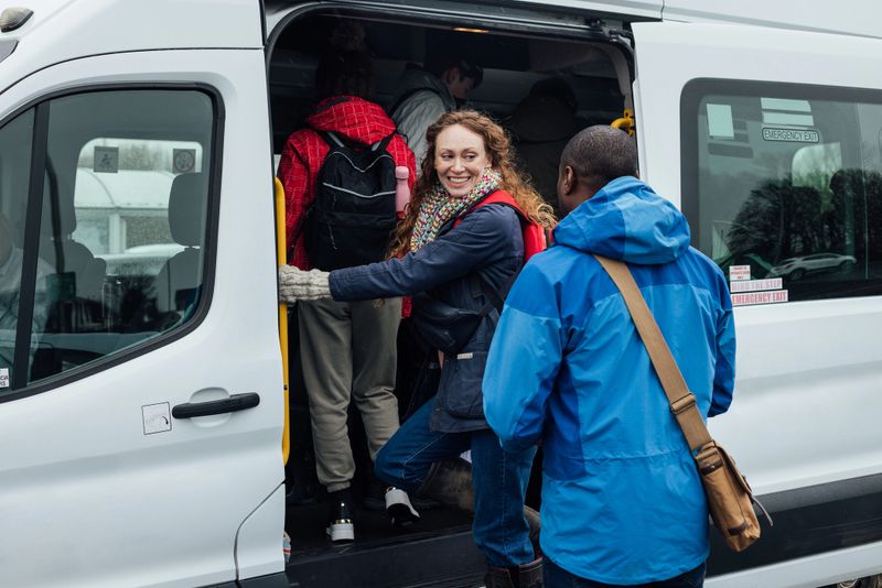 An over the shoulder view of a group of teenage students who are boarding the minibus with their teacher  before heading on a field trip to Rothbury in Northumberland. They are dressed for the weather and keeping warm.