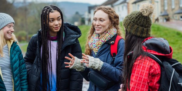Group of four young women chatting outdoors in winter clothes.