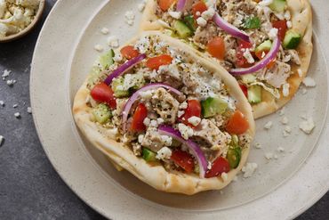 Two pita breads topped with chicken, vegetables, and feta cheese on a plate.