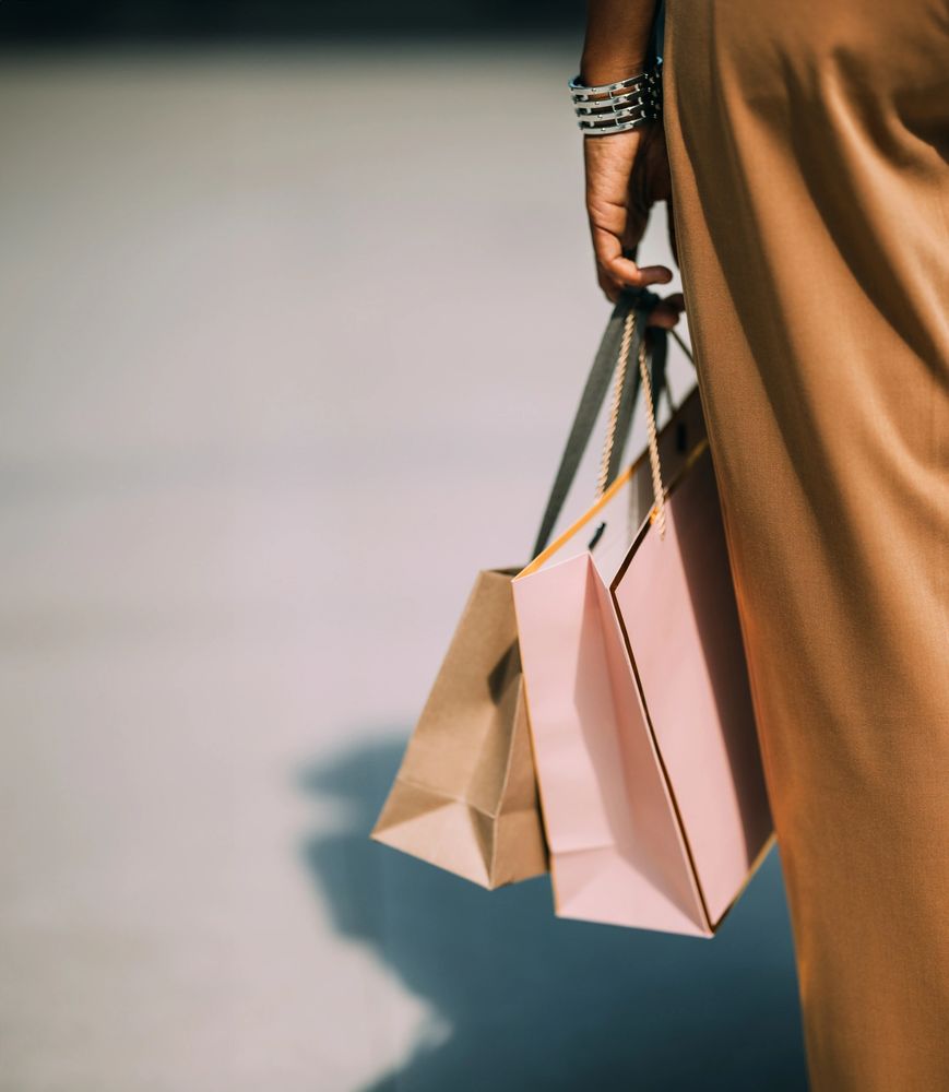 Close-up of a person holding shopping bags while wearing a brown outfit.