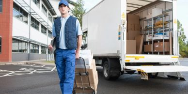 Delivery worker handling packages with a trolley near a truck.