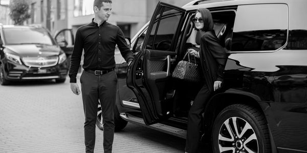 A man opens a car door for a woman stepping out.