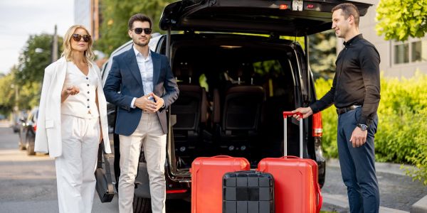 Two travelers meet their driver with three suitcases by a vehicle.