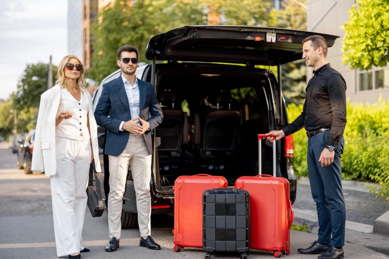 Business couple standing by a minivan taxi waiting for their chauffeur or porter to help them with a suitcases. Concept of business trips and travel