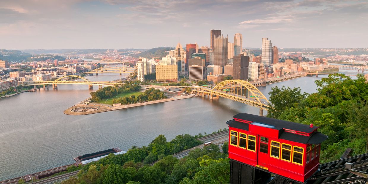 Red incline car overlooking Pittsburgh skyline and rivers at sunset.
