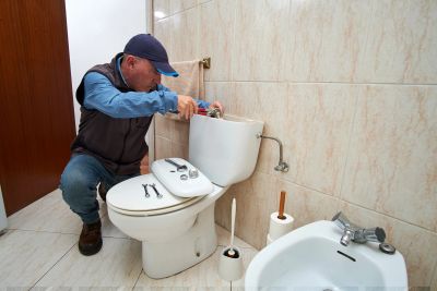 Plumber fixing a toilet tank in a bathroom.