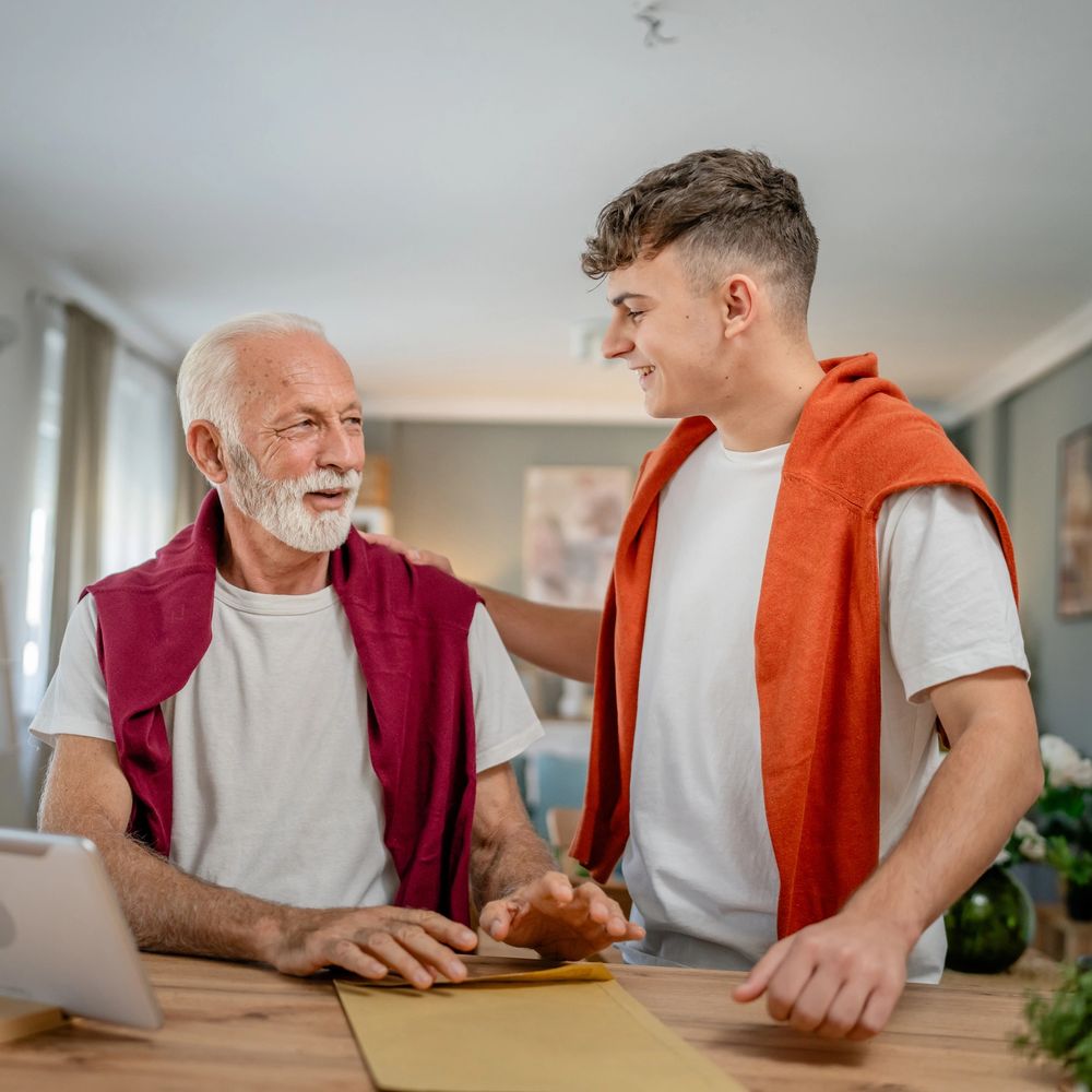 Young man and elderly man sharing a warm moment at a table indoors.