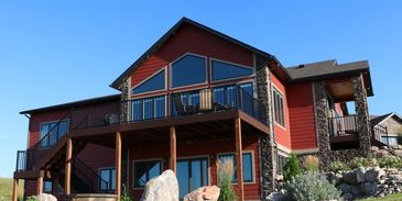 Modern red house with stone accents and a spacious balcony under a clear blue sky.