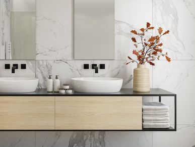 Modern bathroom with marble walls, twin sinks, and decorative autumn branches in a vase.