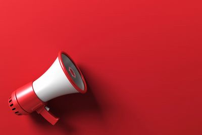 Red megaphone on a red background casting a shadow.