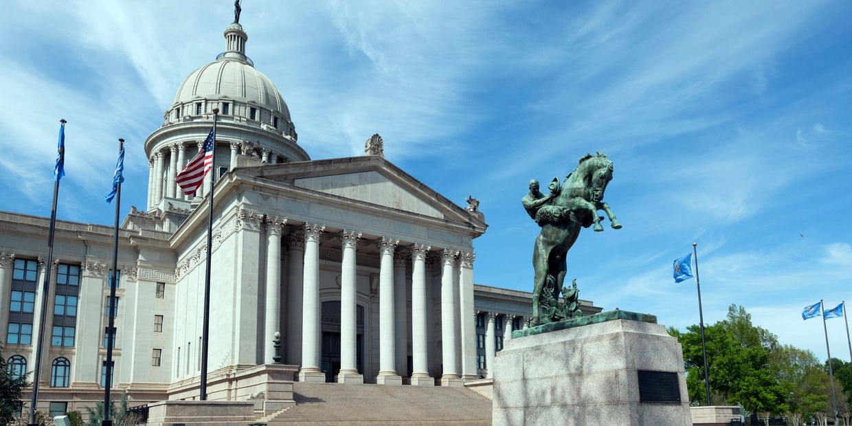 State capitol building with an equestrian statue and flags under a blue sky.