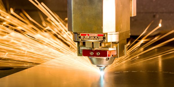 Close-up of laser cutting metal sheet with sparks.