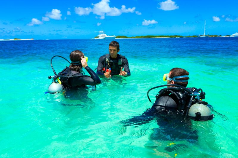 Dive master training a couple for first dive in a tropical turquoise island beach. Travel, relaxing and leisure related themes for vacations in the Caribbean. Image taken at Los Roques, Venezuela. Los Roques is an archipelago or group of small islands located at 80 miles north of the Venezuelan coastline and a very popular destination for leisure, diving, kite surfing and all king of water activities. Los Roques and the beauty of the turquoise coastal beaches of Venezuela are almost indistinguishable from those of the Bahamas, French Polynesia, Malau, Hawaii, Cancun, Costa Rica, Florida, Maldives, Cuba, Fiji, Bora Bora,  Puerto Rico, Honduras, or other tropical vacation travel destinations.