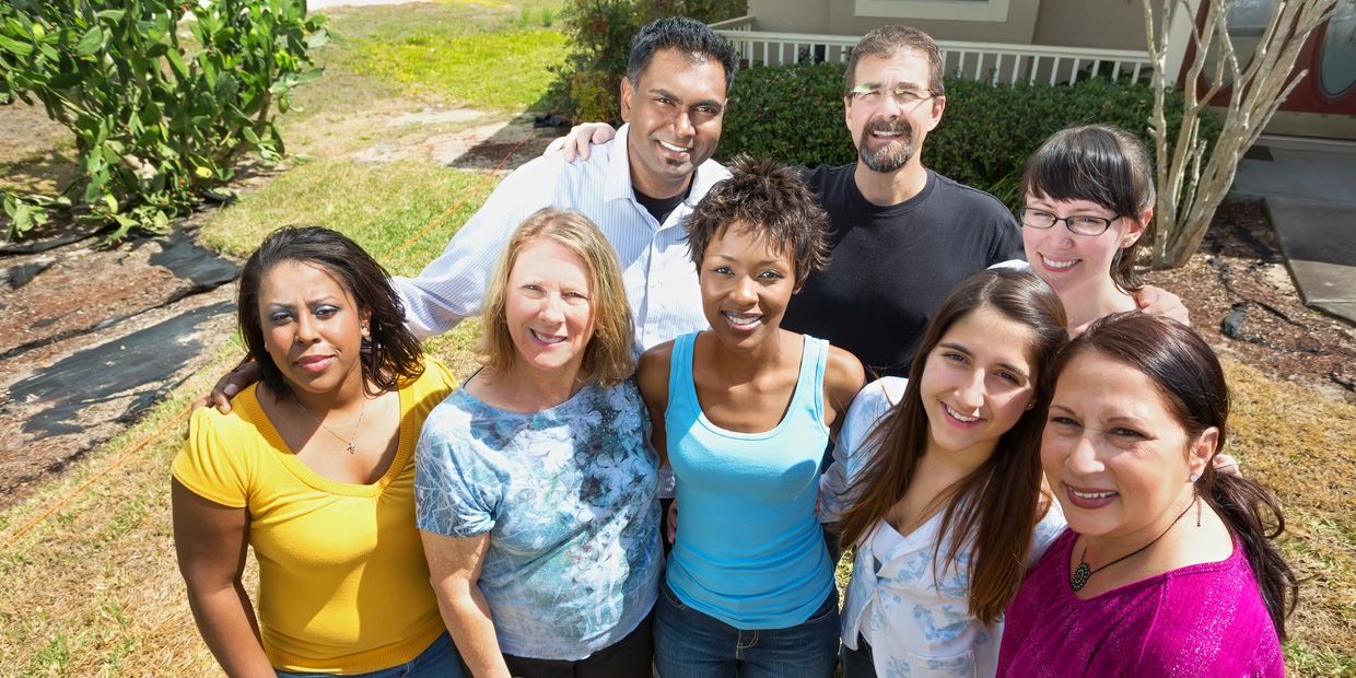 A diverse group of smiling adults posing outdoors on a sunny day.