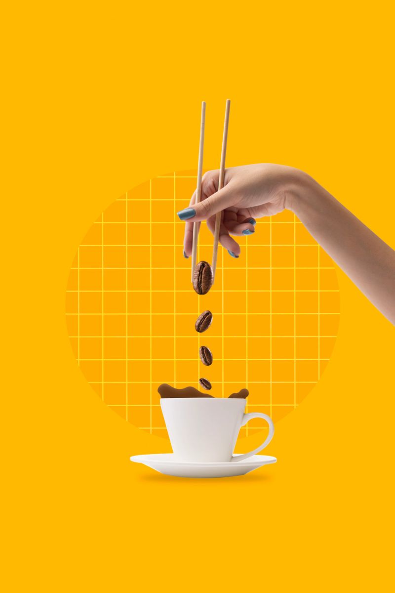 Creative design with female hand holding coffee beans with chopsticks and putting it into coffee cup on yellow background. Concept of drink, taste, art, colorful design. Poster. Copy space for ad.