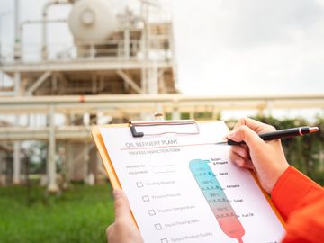 Person holding clipboard with oil refinery plant checklist at industrial site.