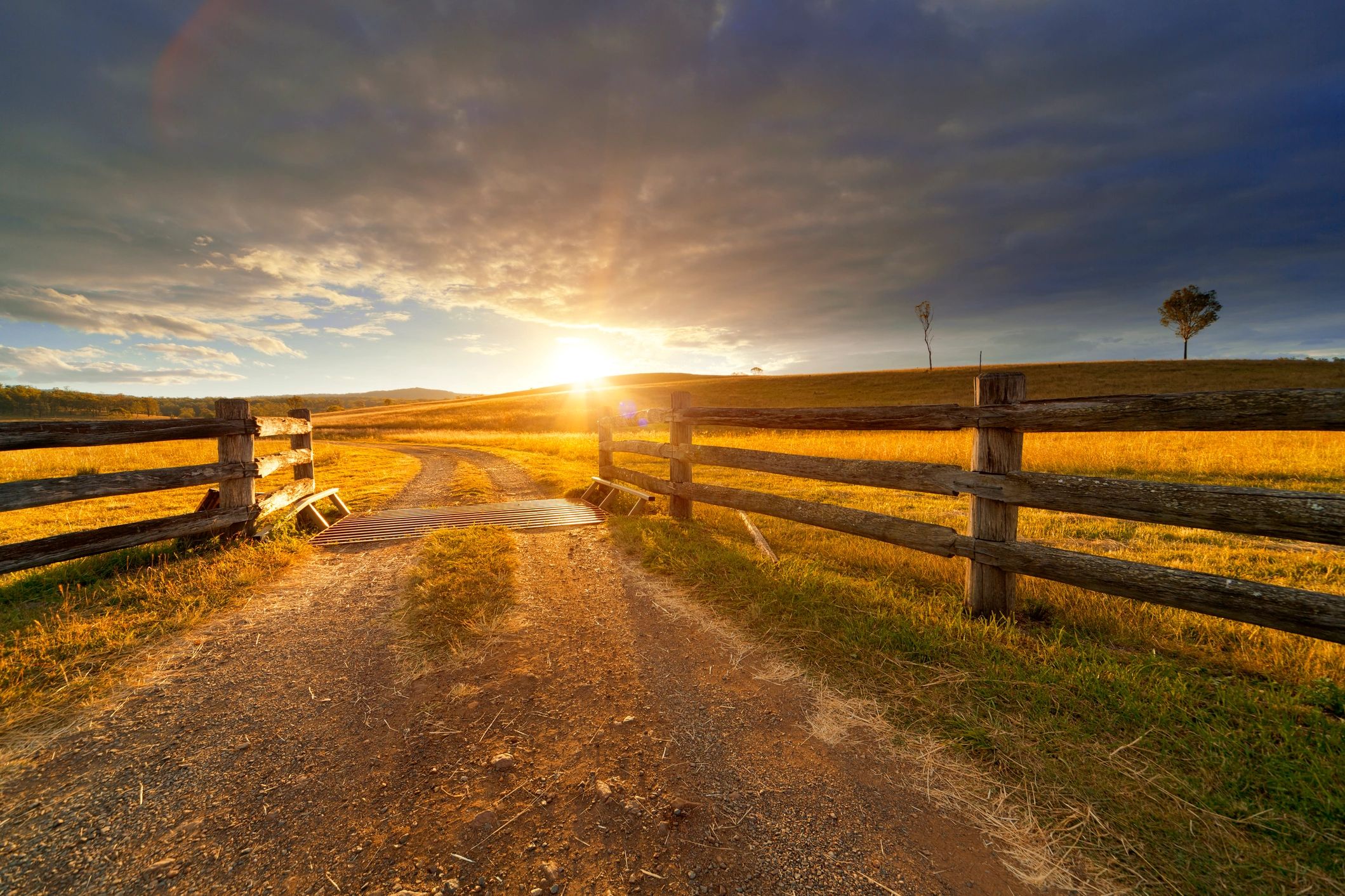 Sunset over a rural fence and dirt road.