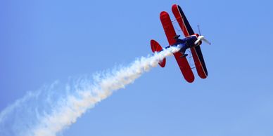 Red biplane doing aerial maneuvers with smoke trail.