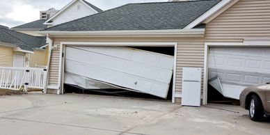 Two damaged garage doors on a beige house with a refrigerator outside.