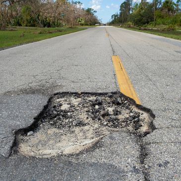 Large pothole in the middle of a rural road with a yellow centerline.