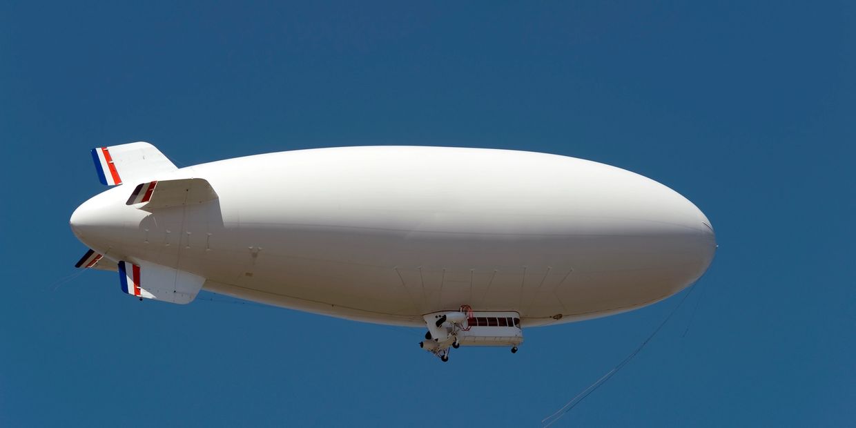 A white blimp flying against a clear blue sky.