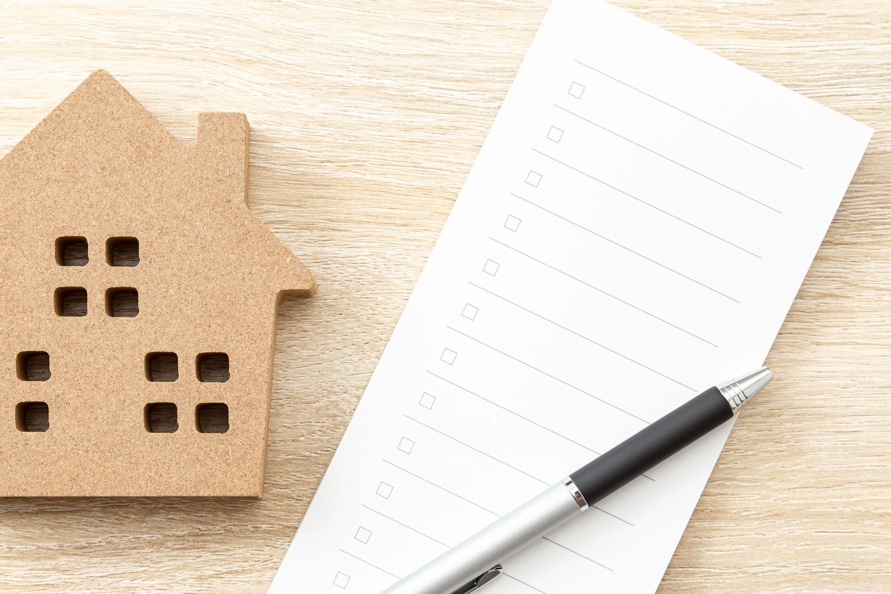 Wooden house model with checklist and pen on table.