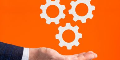 Hand holding white gears against an orange background.