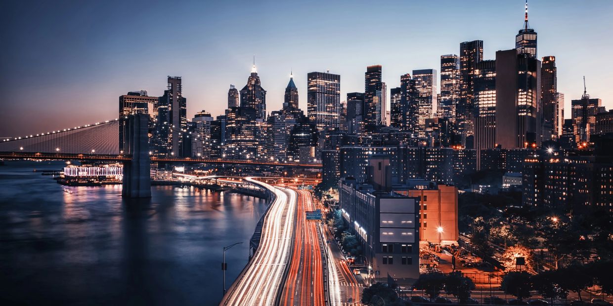 Nighttime cityscape with illuminated skyscrapers and light trails on a busy highway.