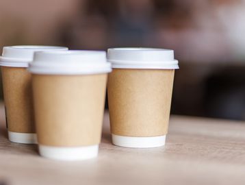 Three disposable coffee cups with white lids on a wooden surface.