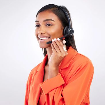 Smiling woman in orange jacket wearing a headset and speaking.