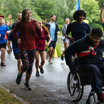 Diverse group joyfully running and celebrating outdoors, including a man in a wheelchair.