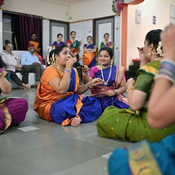 Women in traditional attire singing and enjoying a cultural gathering indoors.