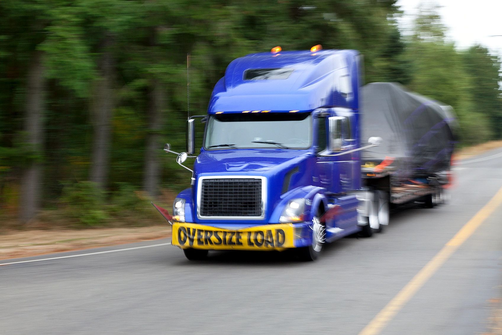 Blue truck with 'Oversize Load' sign moving fast on road.