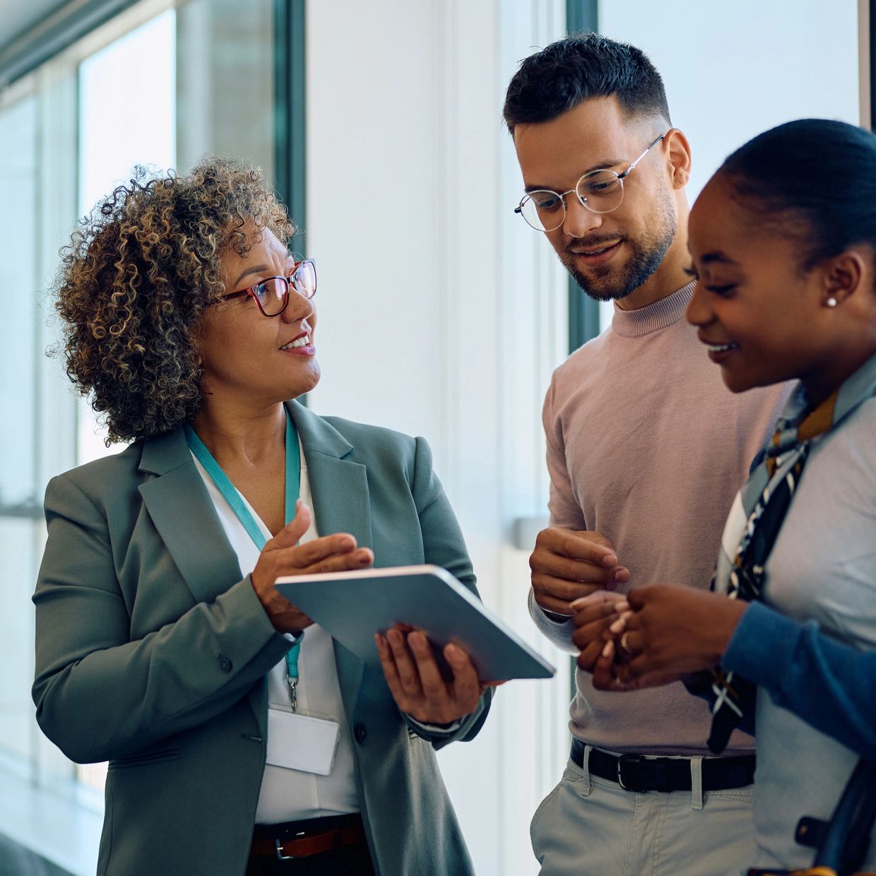 Three colleagues discussing work using a digital tablet in a modern office.
