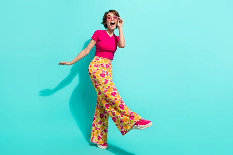 Full length photo of cute impressed woman dressed flower print trousers having fun empty space isolated teal color background.