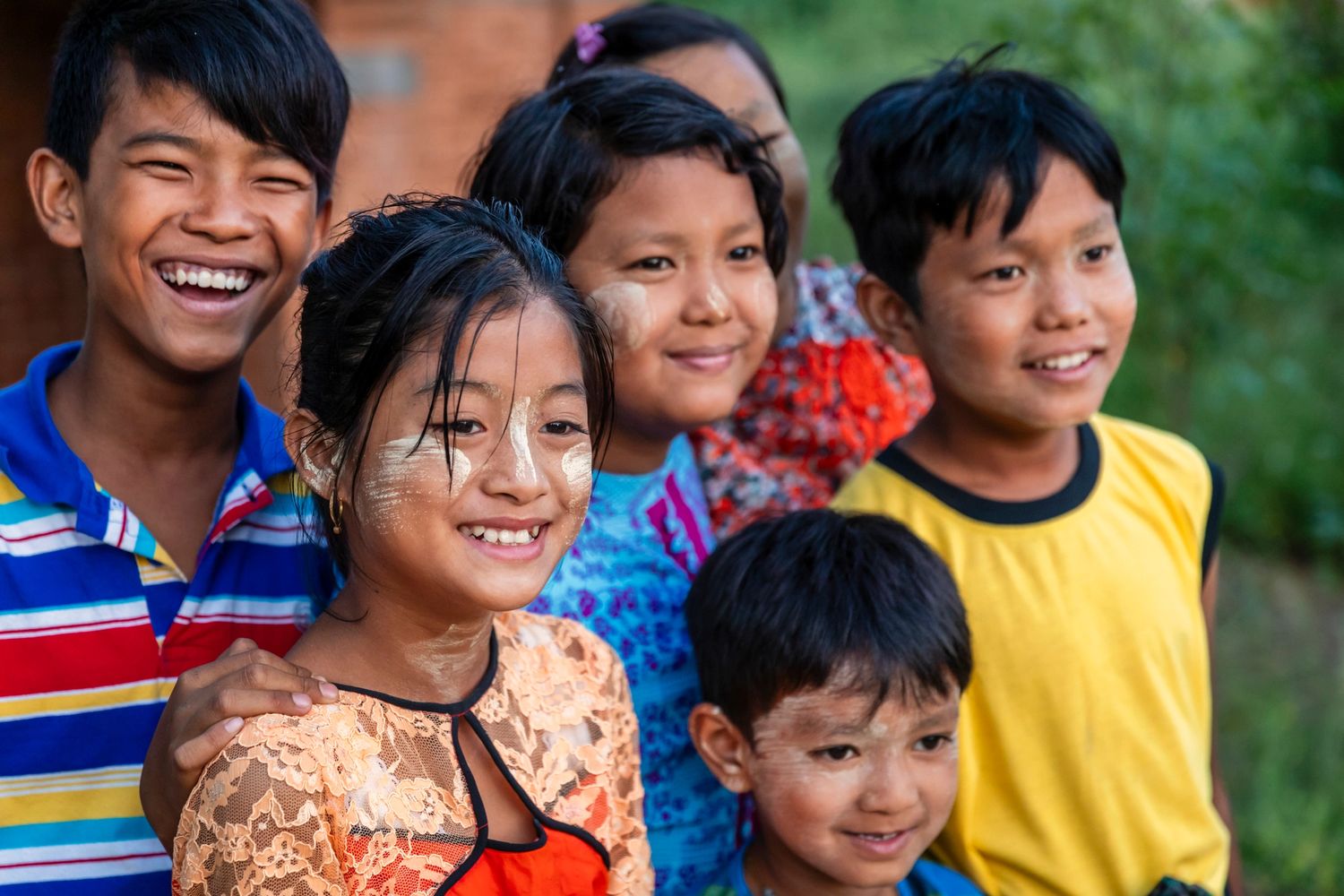 A group of smiling children with traditional face paint, enjoying time together outdoors.