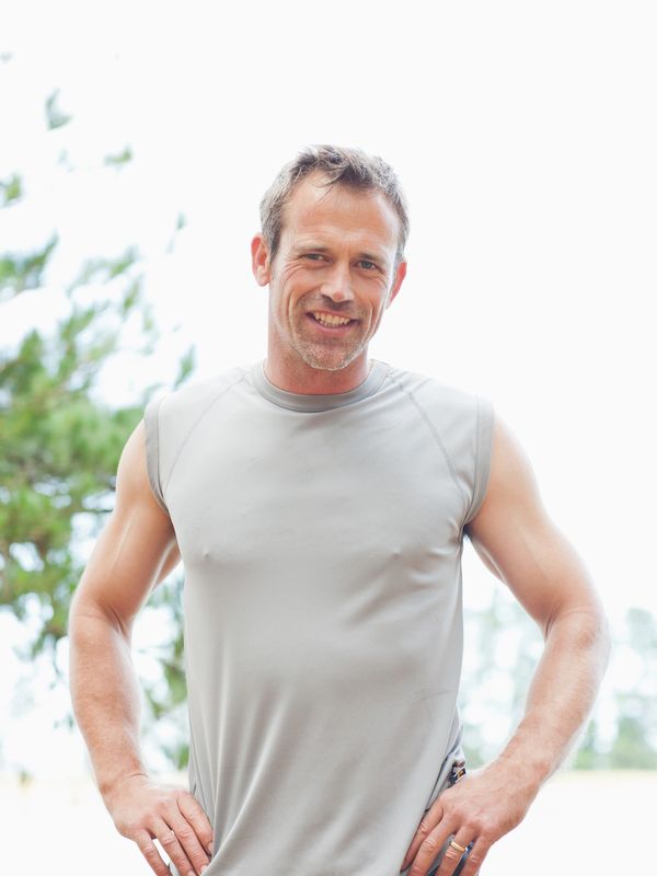 Smiling man in sleeveless gray shirt outdoors.