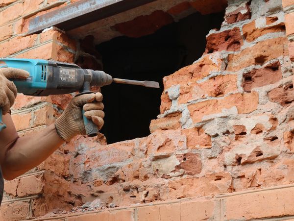 Worker using a drill to break a brick wall.