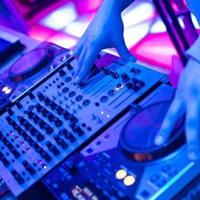 DJ hands adjusting controls on a mixer with vibrant blue and pink lighting.