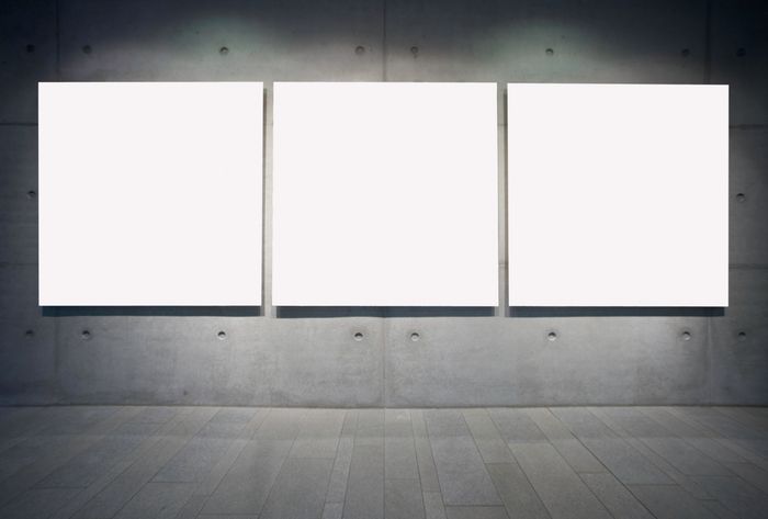 Three blank white canvases hang on a gray concrete gallery wall.