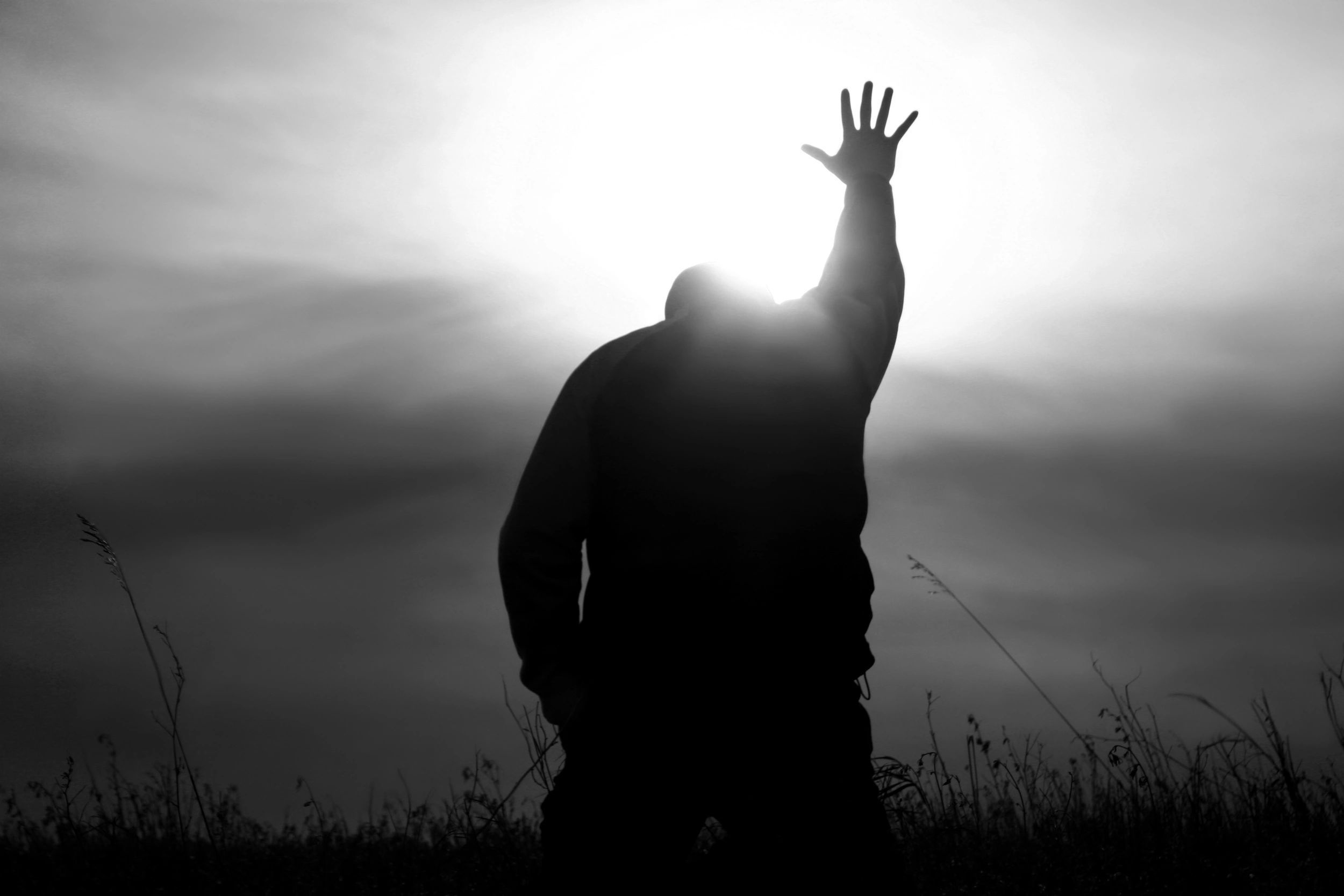 Silhouette of a person raising hand towards the bright sun in a field.
