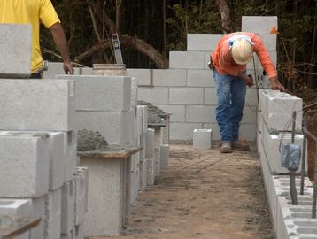 Construction workers building a concrete block wall outdoors.