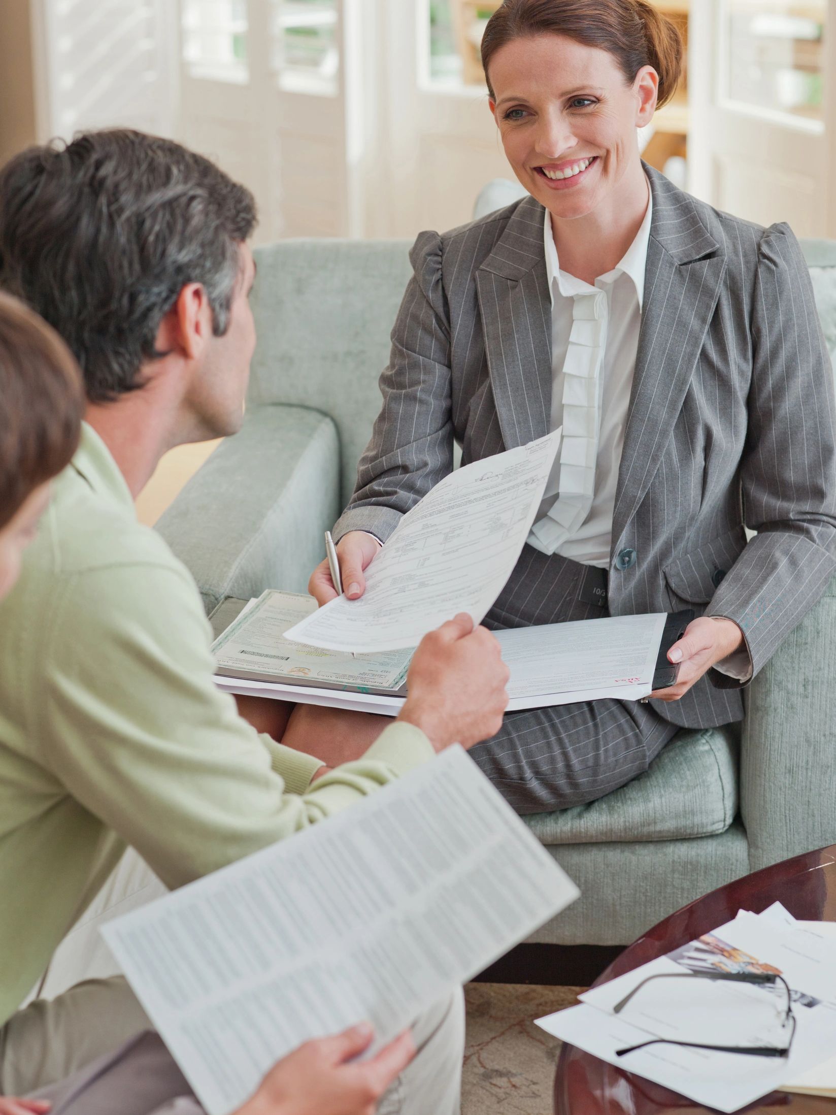 Woman in suit discussing documents with a couple on a sofa.