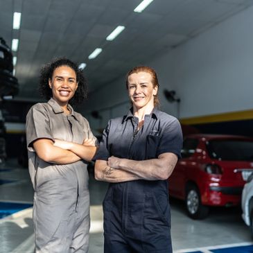 Two female mechanics standing confidently in a garage with arms crossed.