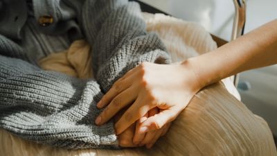 Two people holding hands, one in a gray sweater, sharing a comforting moment.