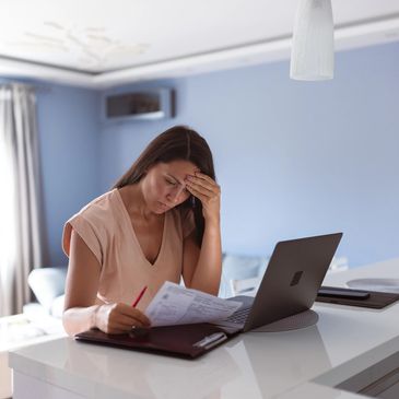 Woman stressed while working with documents and laptop.